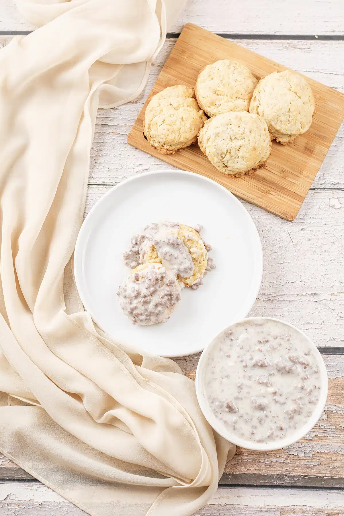 Sausage gravy on a small plate with a board of golden biscuits behind