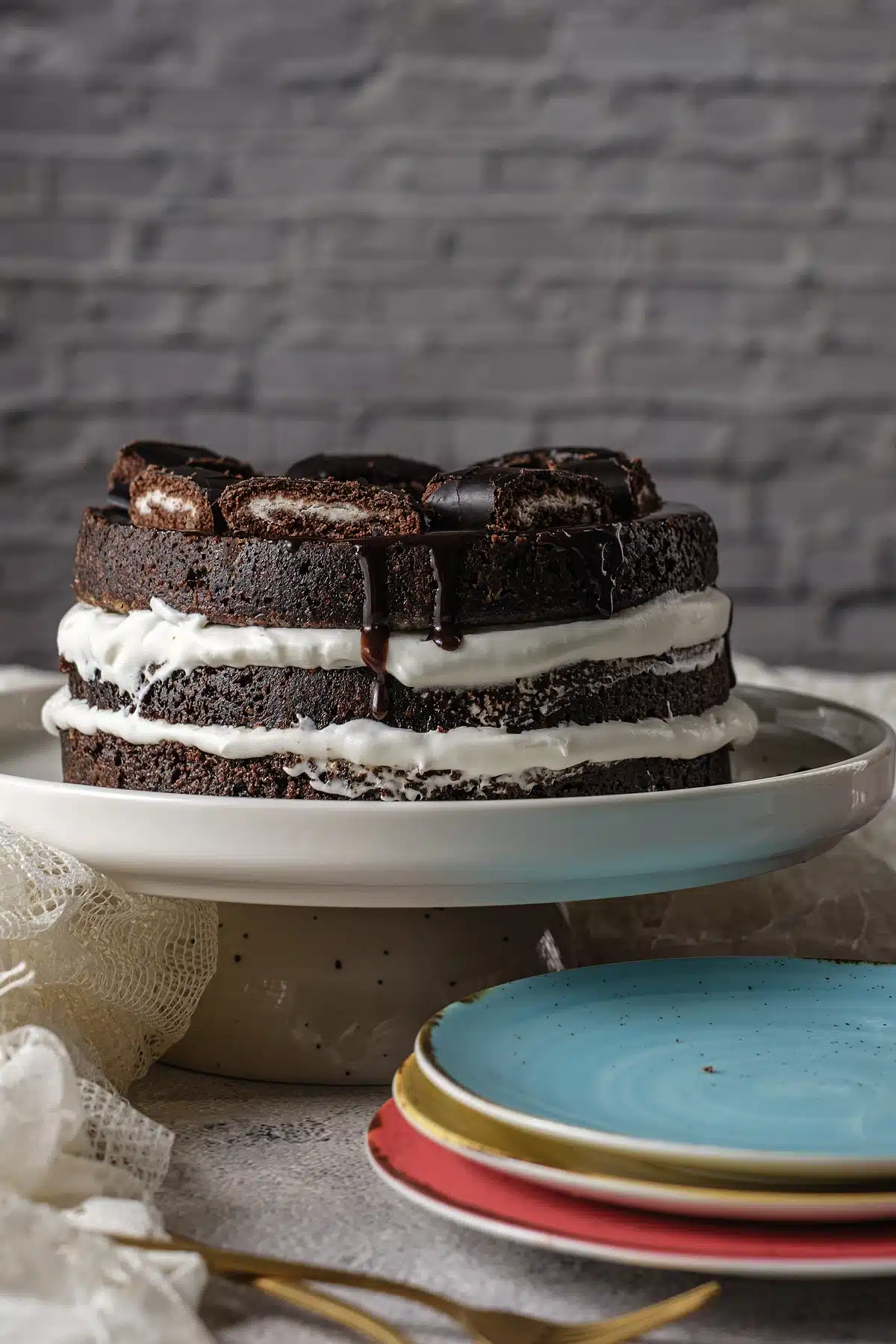 Ho ho cake standing tall on a white stand against a gray brick wall