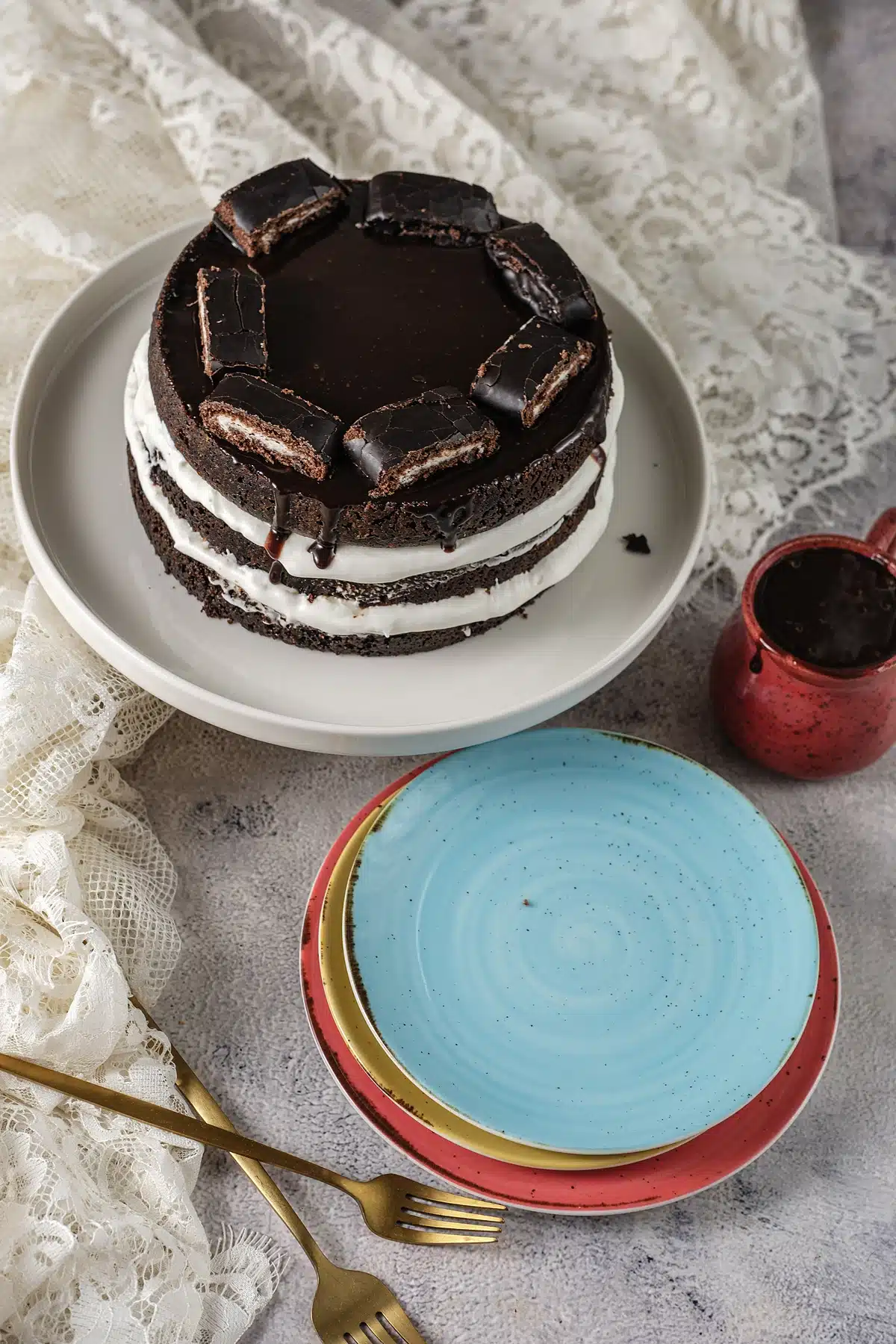Ho ho cake on a stand beside a small red jug of ganache and stacked plates