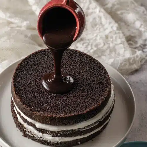 A hand tipping dark glaze from a red jug over the top of the stack