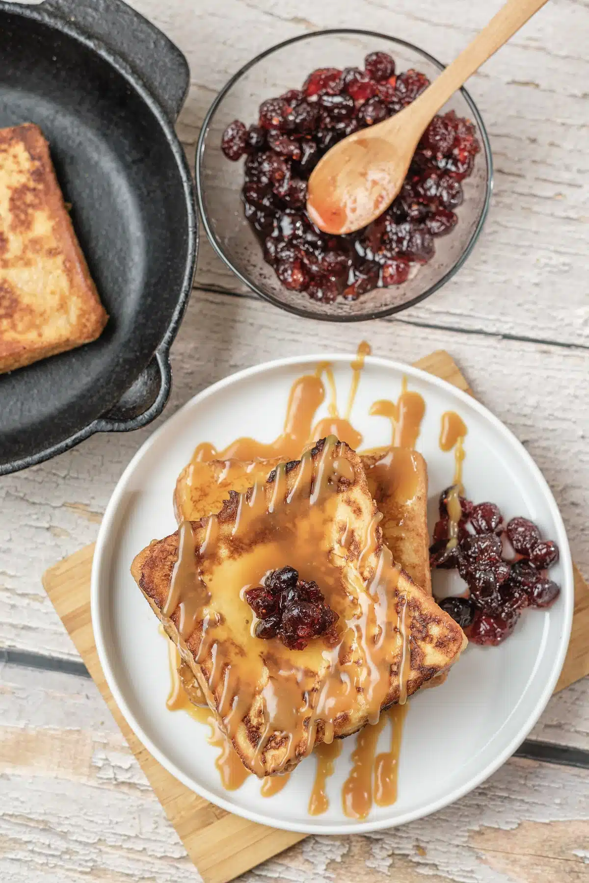 IHOP French toast with caramel drizzle and dried cranberries on a white plate, with a skillet of slices behind