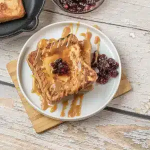 A single serving of IHOP French toast with caramel drizzle and dried cranberries on a white plate