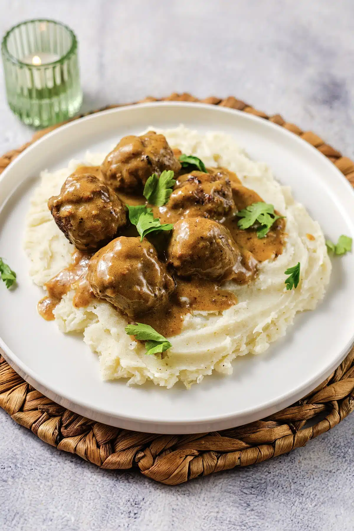 A wide plate of gravy and mashed potato on a woven mat with a candle behind