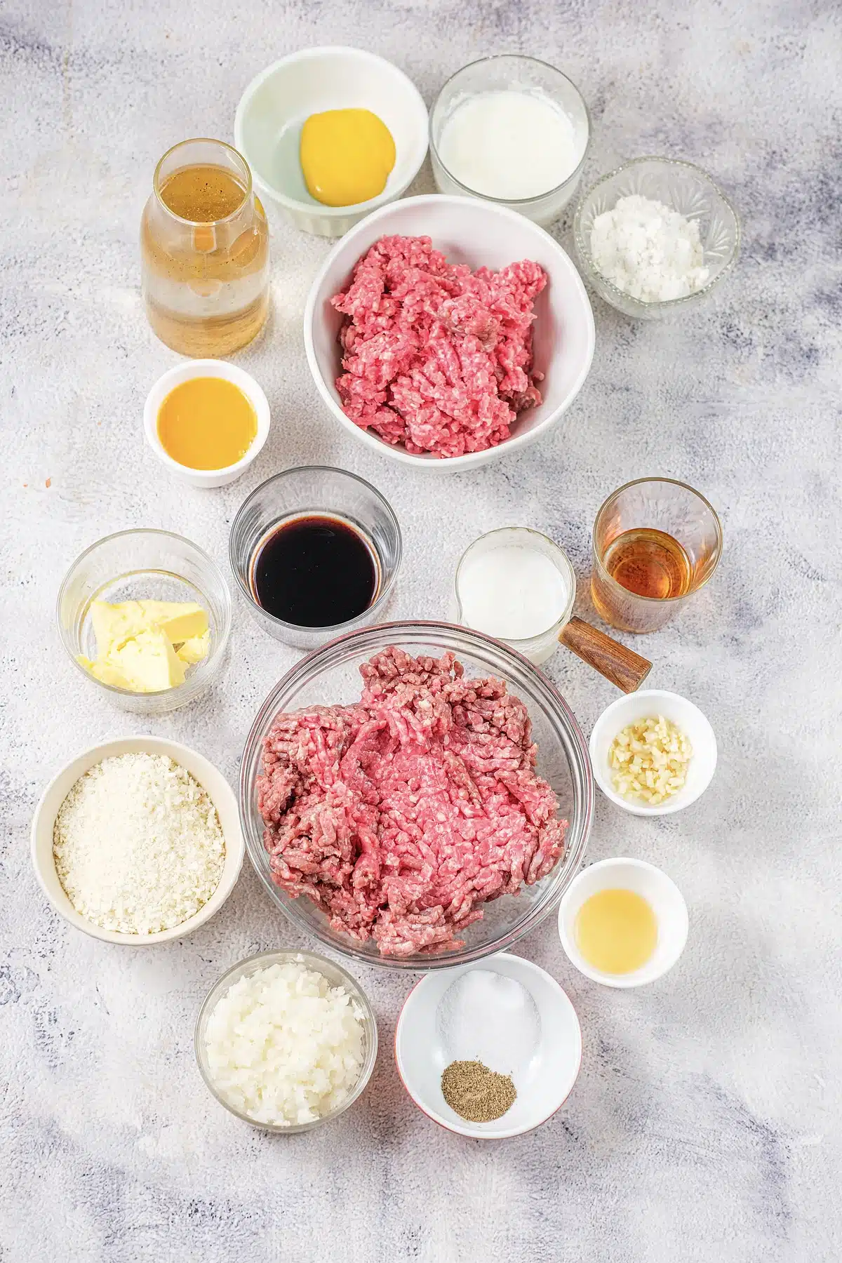 Two bowls of ground meat with breadcrumbs, cream, butter, stock and seasonings around them