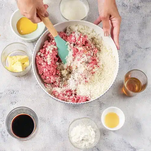 Hands folding the meat and crumbs together with a spatula