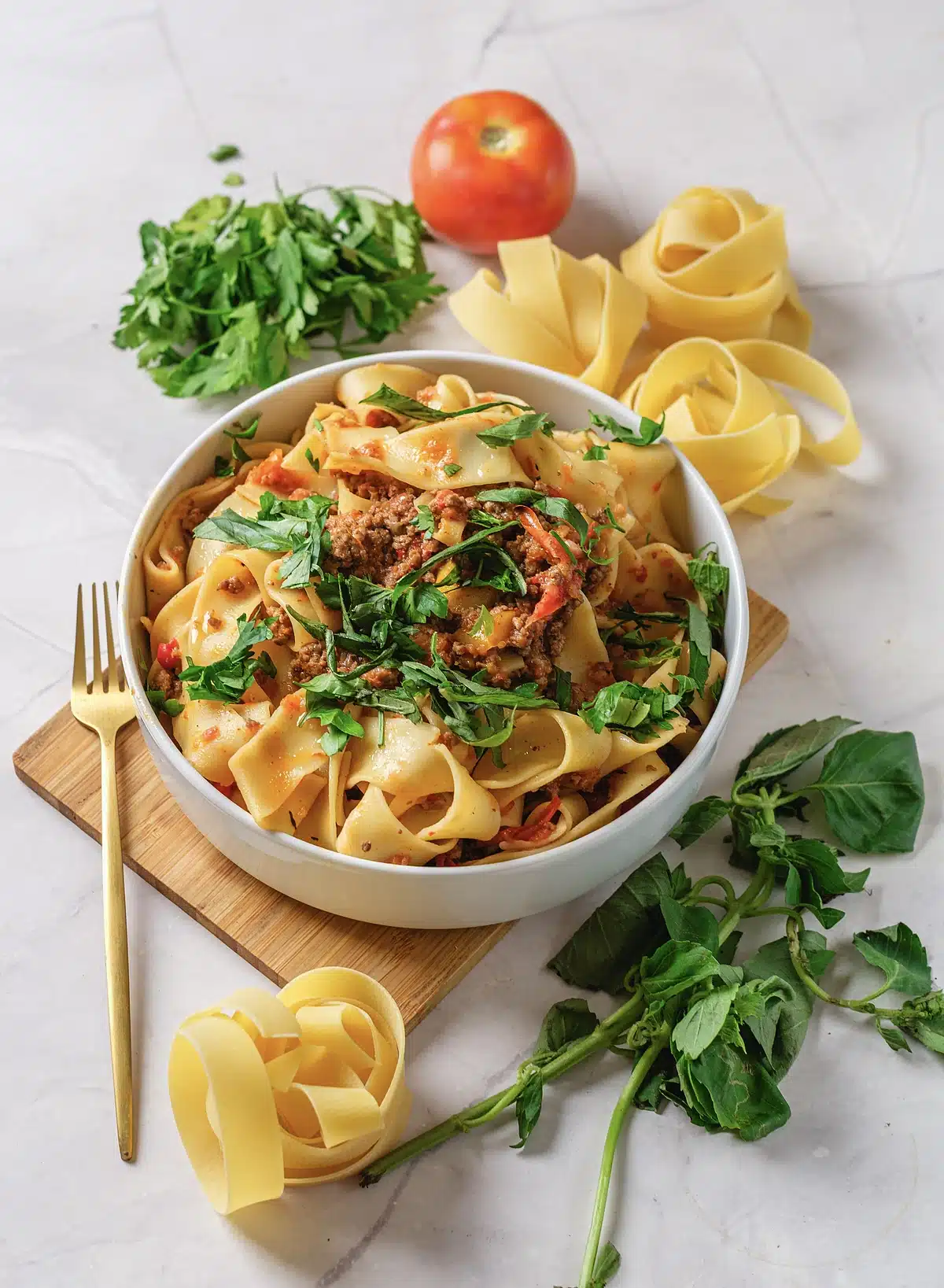 Italian drunken noodles in a white bowl on a wooden board with a gold fork