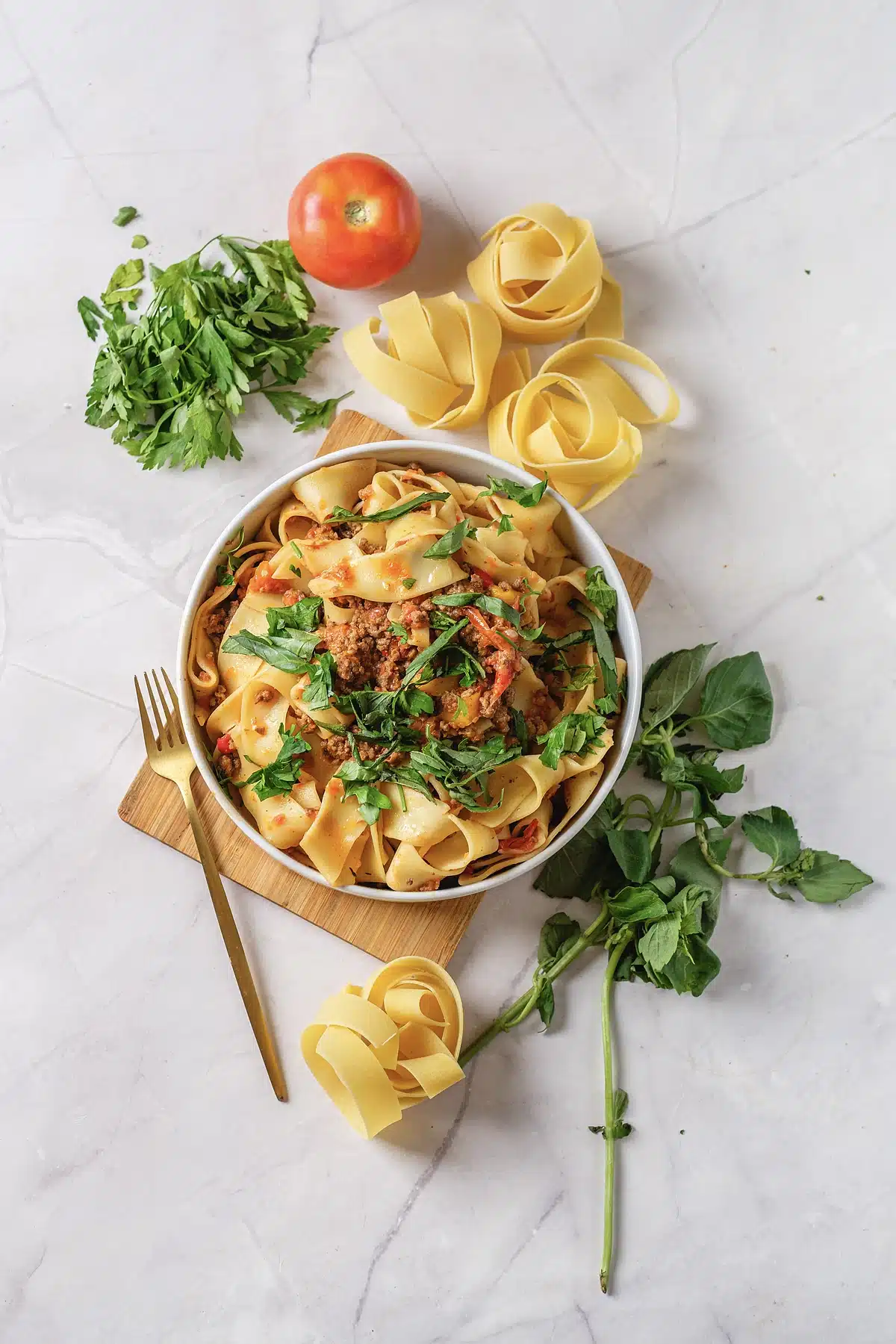 Italian drunken noodles served in a small bowl with parsley and a tomato alongside