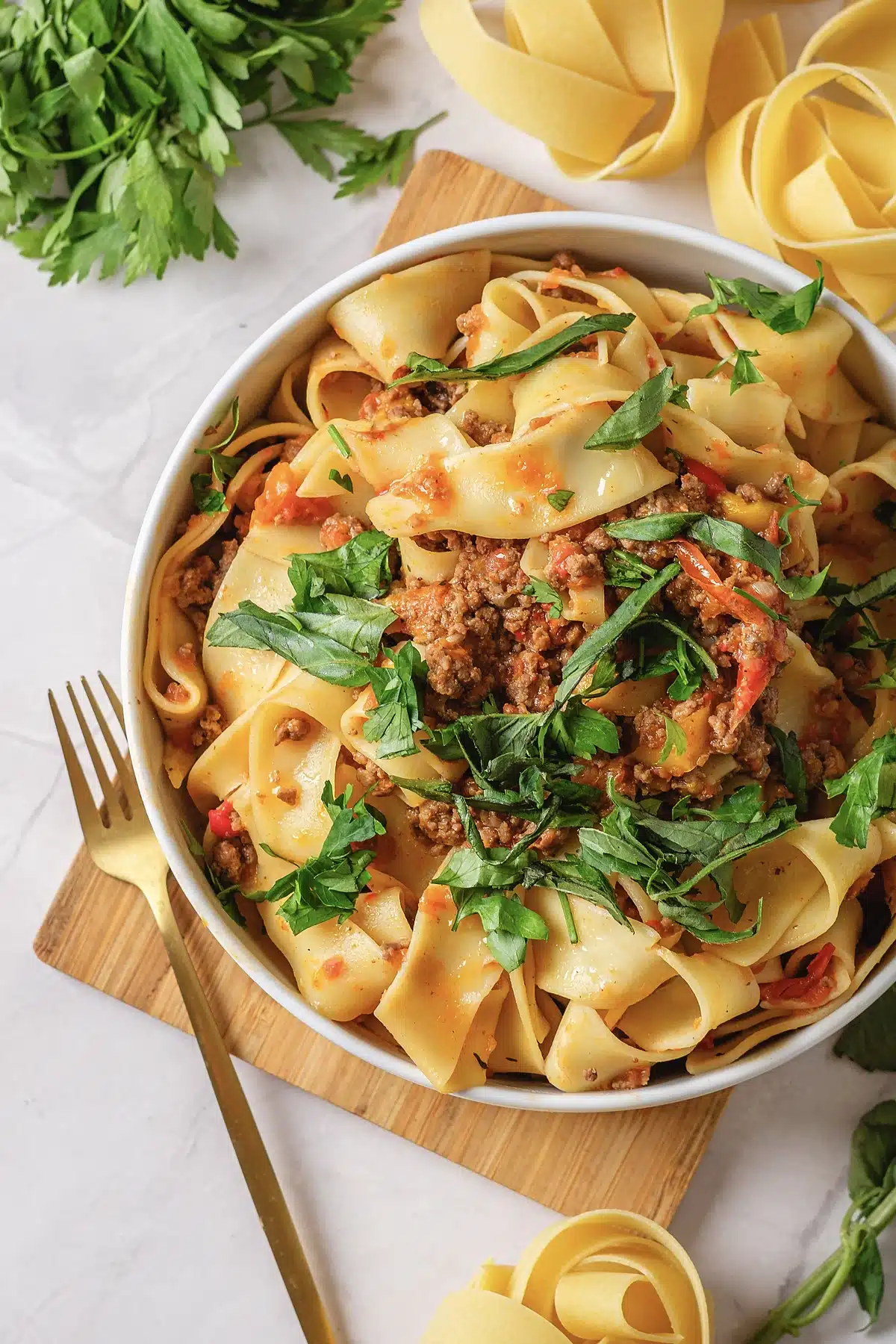 Italian drunken noodles in a wide bowl with a gold fork and herbs alongside