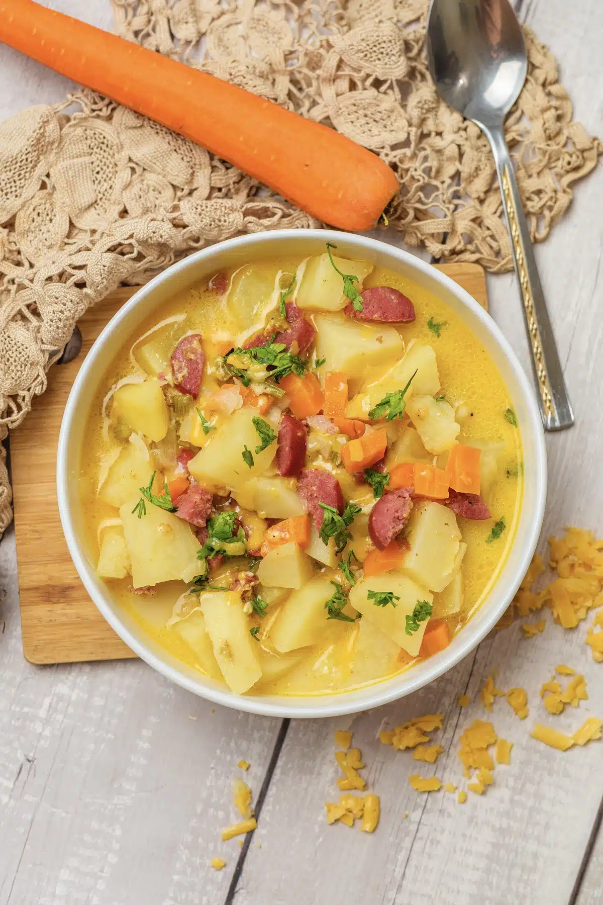 Kielbasa potato soup in a white bowl from above, with large potato chunks, small pieces of sausage, carrot and parsley