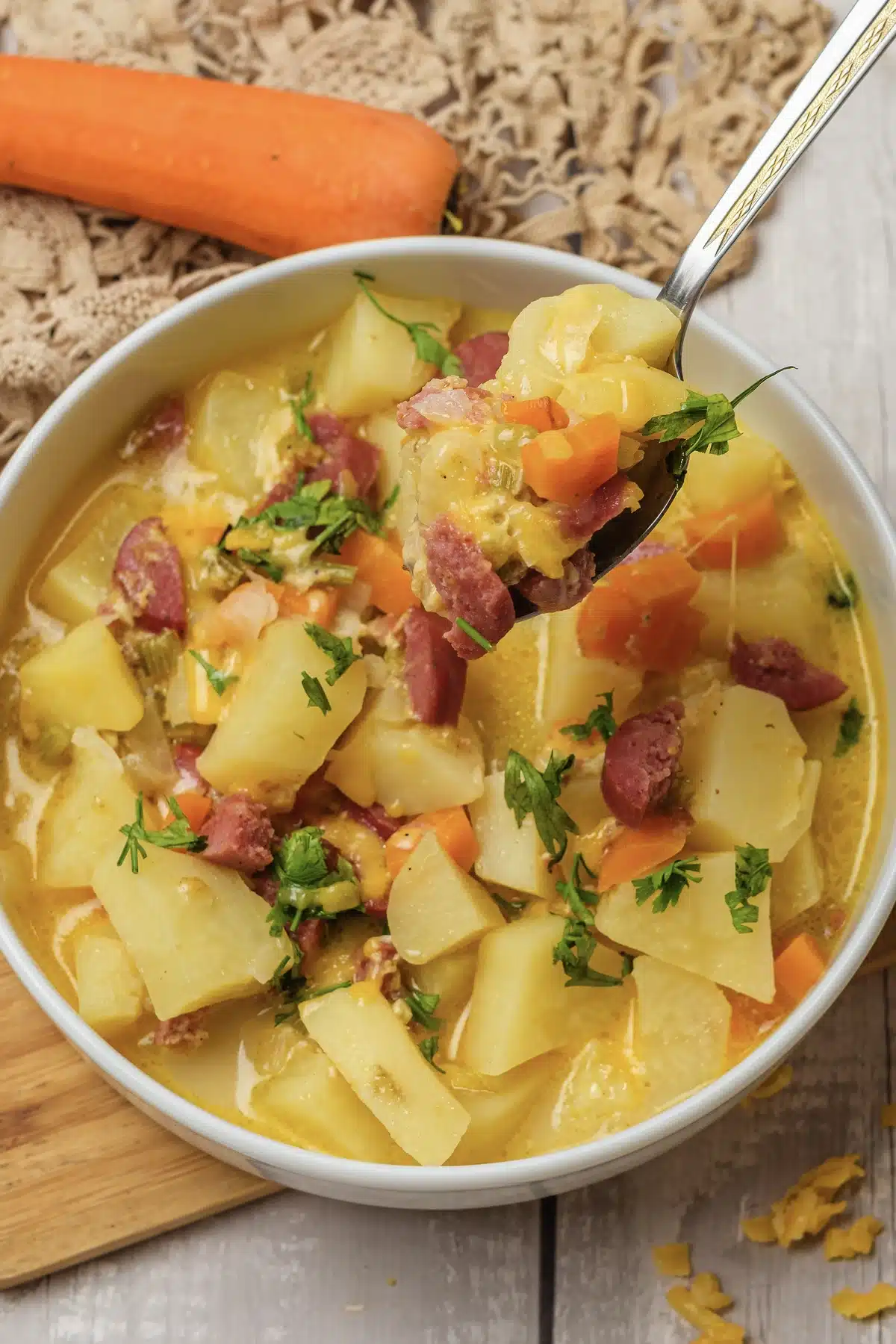 A close spoonful of golden broth, sausage pieces and carrot lifted over the bowl