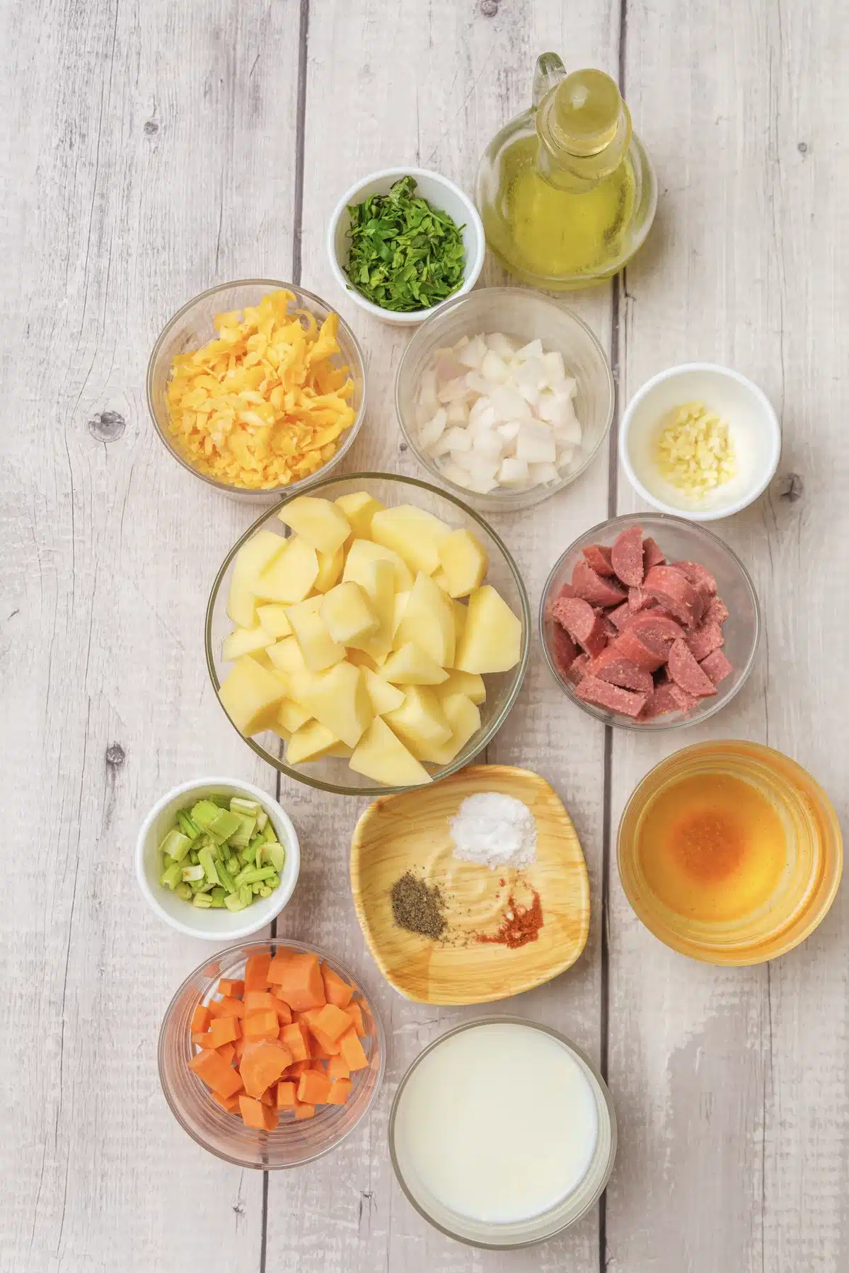 Diced kielbasa, cubed potatoes, carrot, celery, onion, garlic, cheddar, cream, broth, olive oil, parsley and spices in bowls