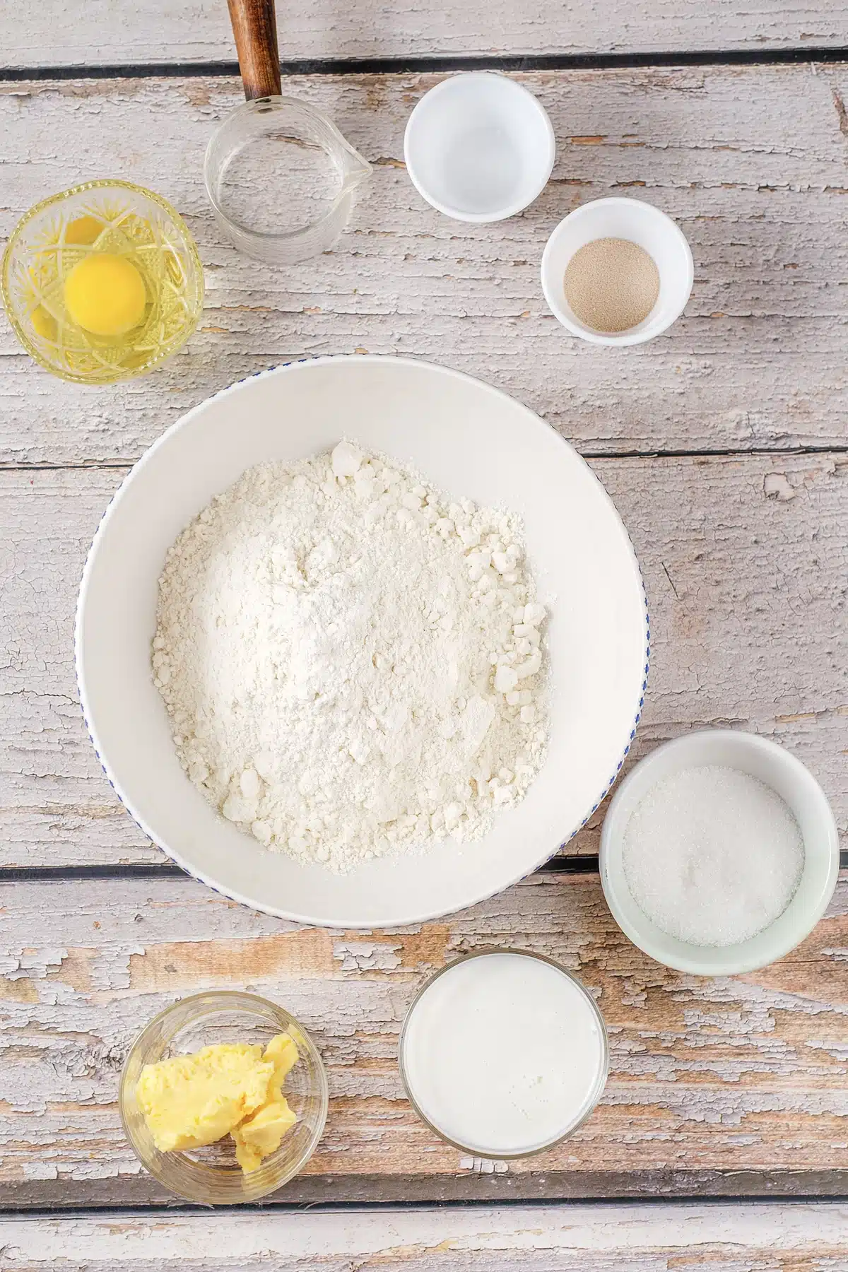 Flour, milk, eggs, butter, sugar and yeast measured into bowls on a pale table
