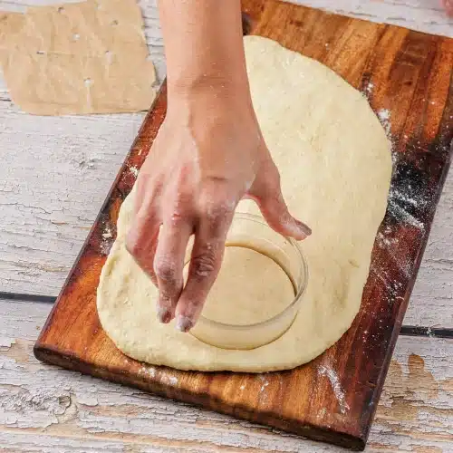 A hand pressing a round cutter into the rolled dough