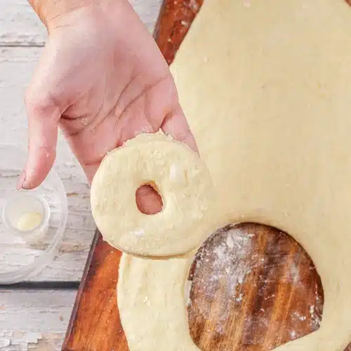 A hand lifting a freshly cut ring away from the sheet of dough