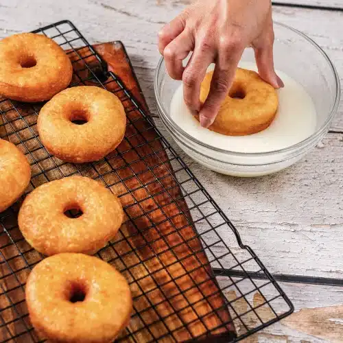 A hand dipping a warm ring face down into the bowl of glaze