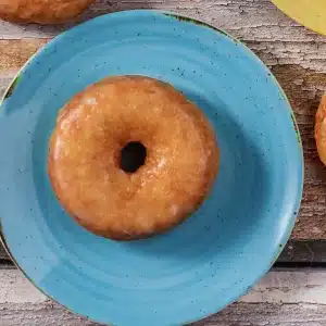 A single glazed donut centered on a blue speckled plate