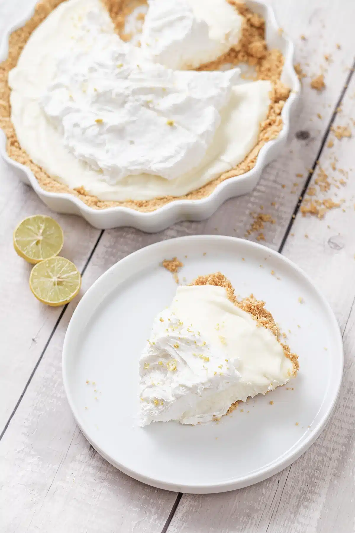 Lemon icebox pie with a wedge on a white plate and crumbs on the wood