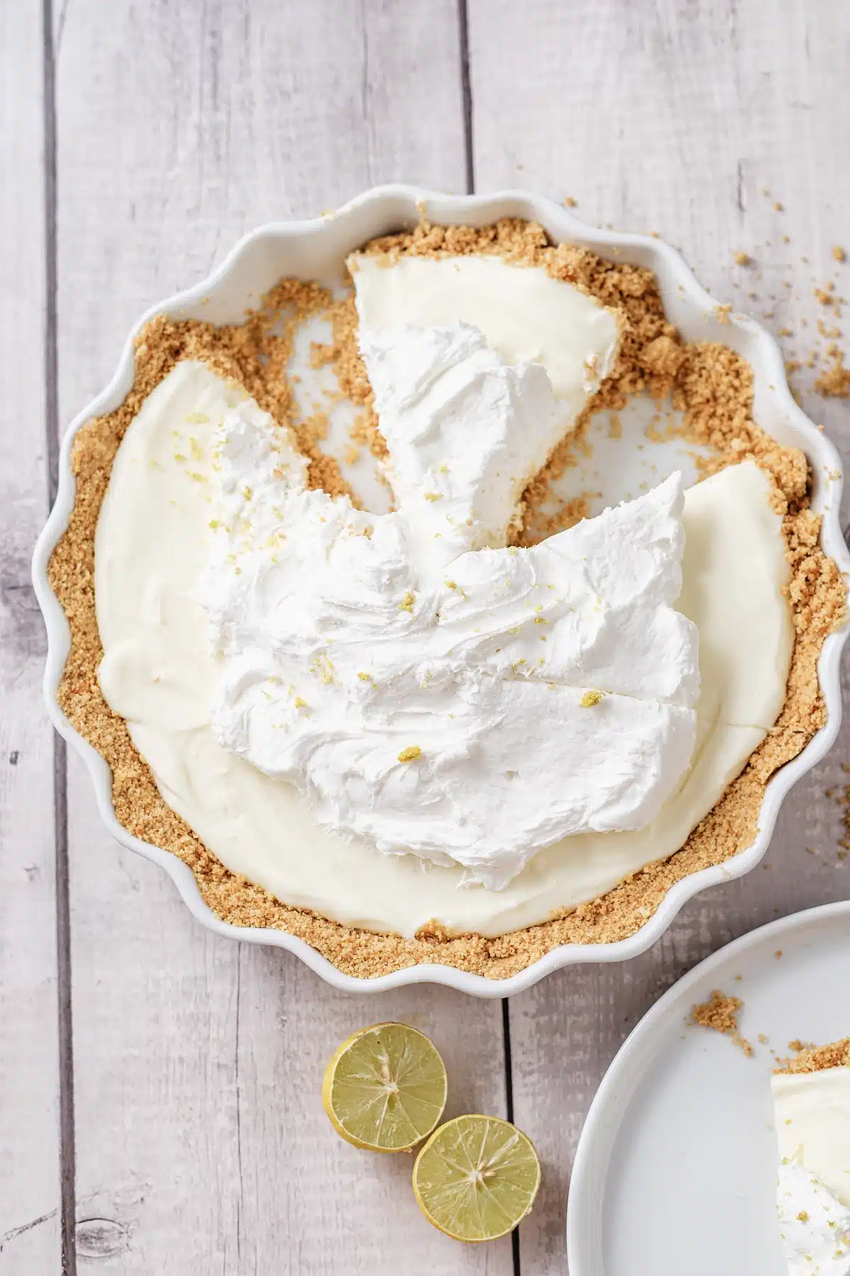 Lemon icebox pie seen from above with slices cut and lime rounds alongside