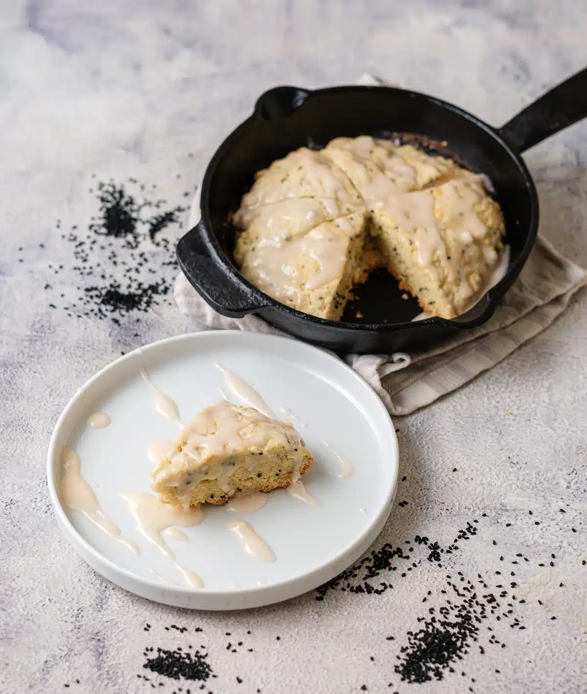 One wedge of lemon poppy seed scones on a white plate with the skillet behind it