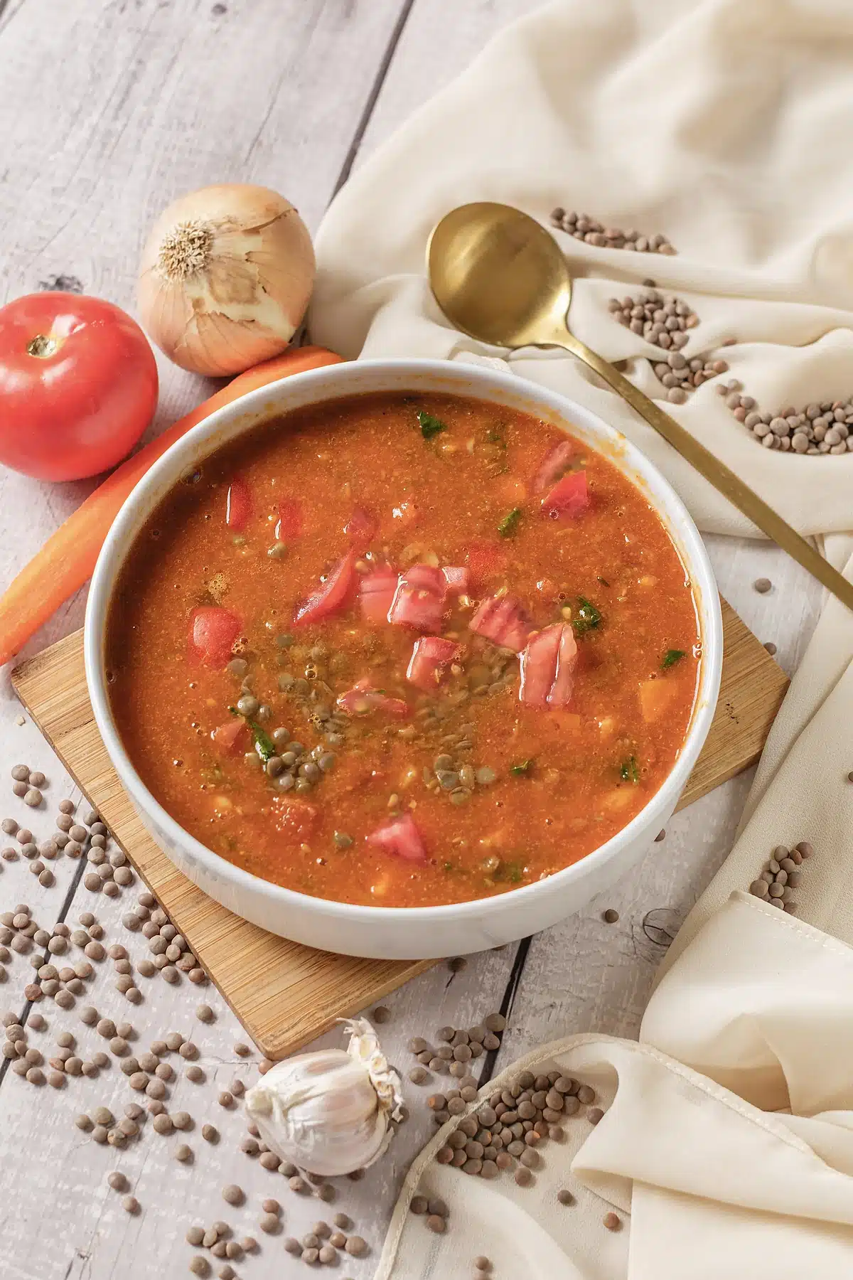Lentil soup in a white bowl with diced tomato and a gold spoon