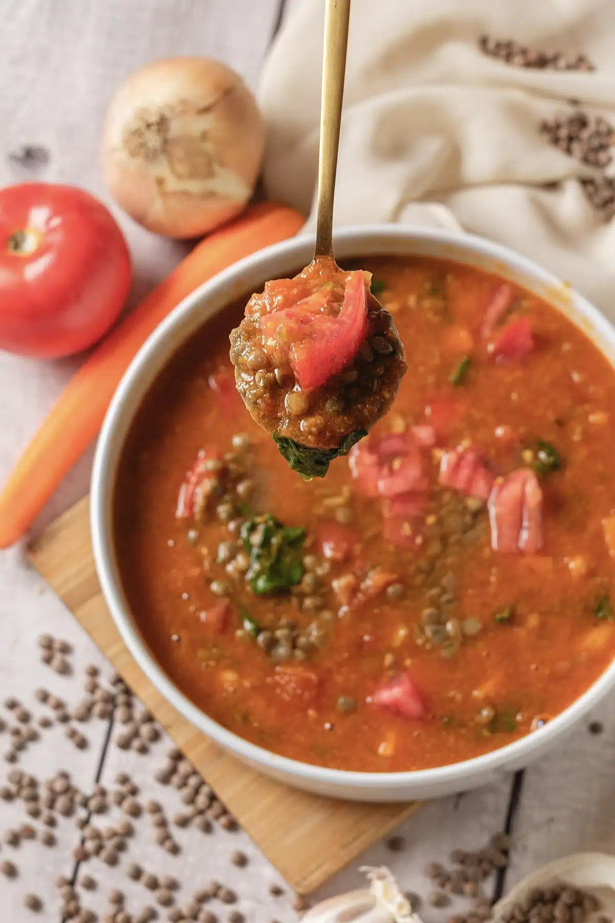 Lentil soup on a wooden board with a spoonful raised over the bowl