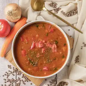 A single bowl of lentil soup topped with diced tomato and herbs