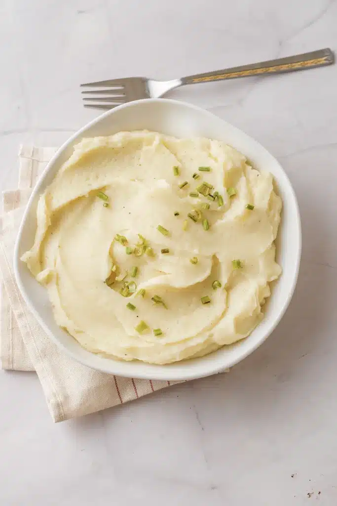 Mashed rutabaga, the pale half-potato version, in a white bowl with chives and a fork, seen from directly above