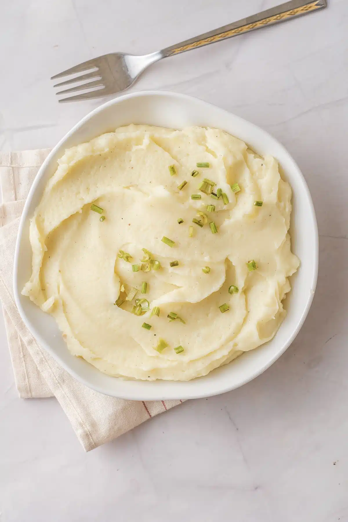 Mashed rutabaga, the half-potato version, swirled in a white bowl with chopped chives and a fork