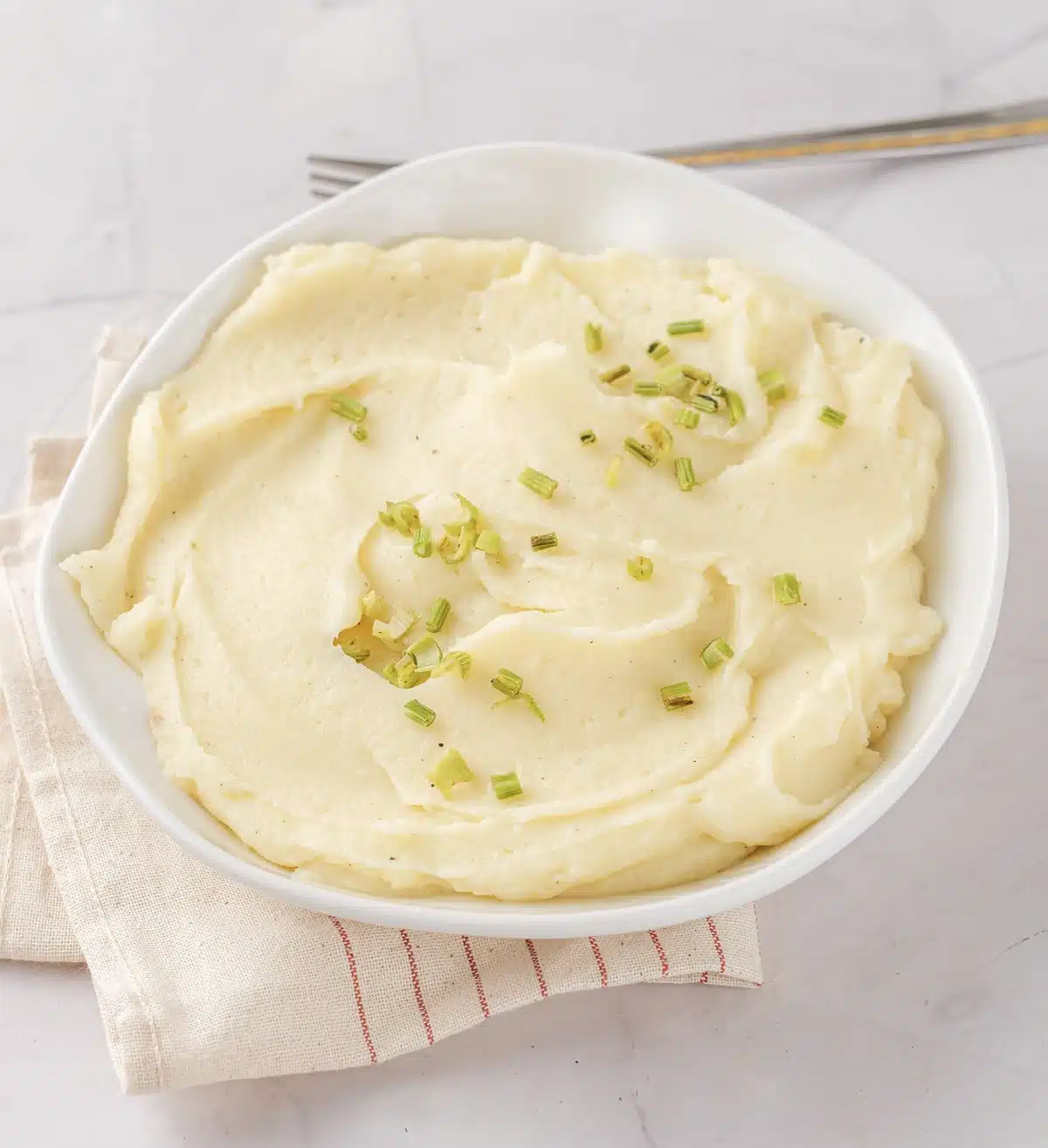 A close view of the creamy pale swirl in a white bowl with chives and a fork resting on the rim
