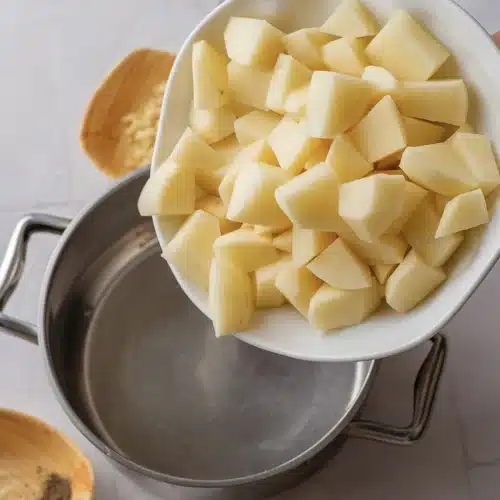 Peeled pale yellow cubes tipped from a white bowl into a steel pot