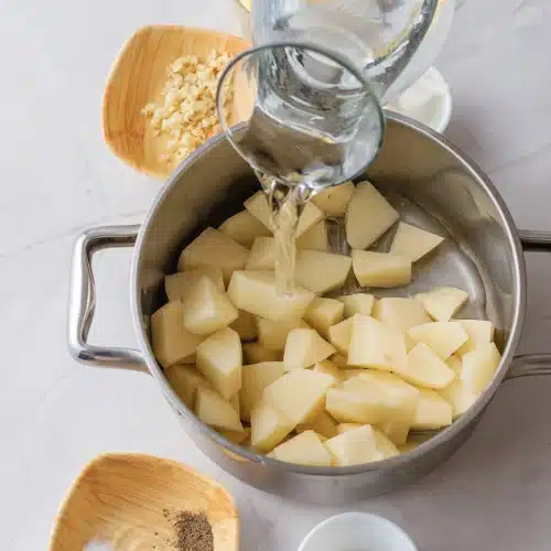 Water poured from a glass jug over the cubes in the pot