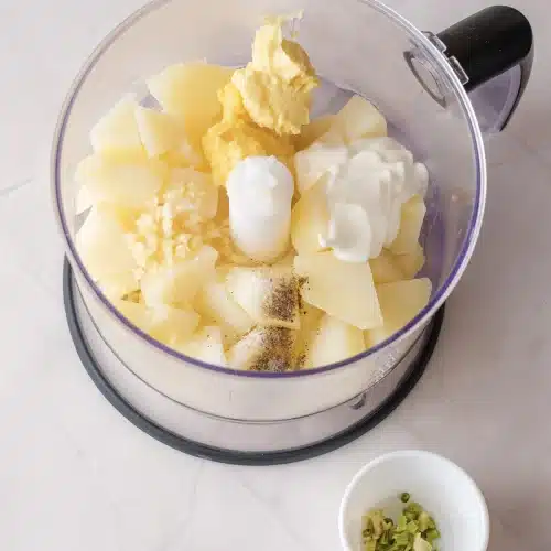 Cooked cubes in a food processor bowl with butter, minced garlic and sour cream on top
