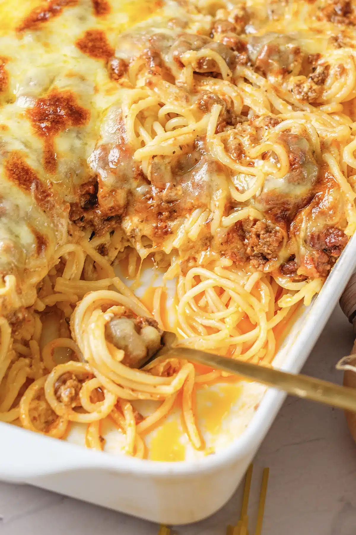 A fork twirling strands under a blistered cheese crust