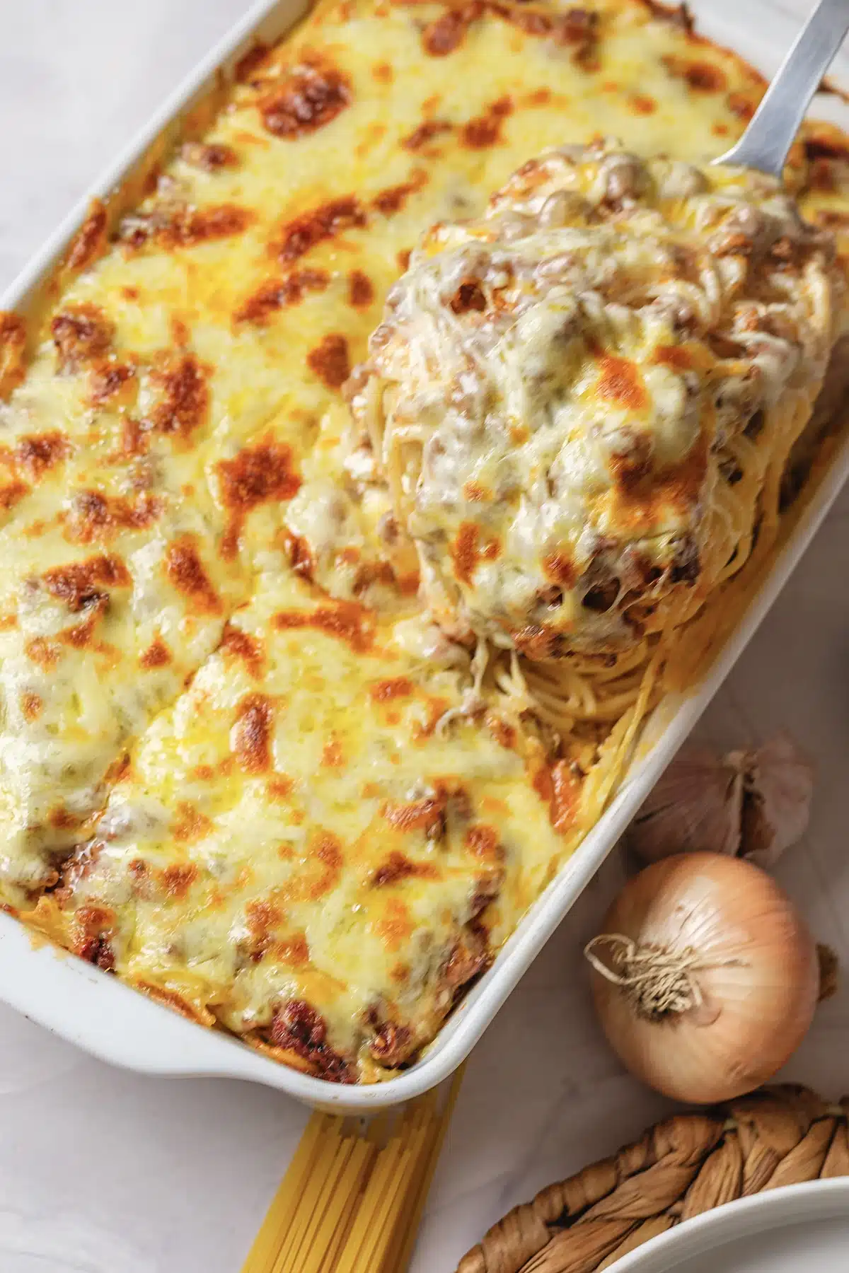 A serving spoon lifting a cheesy portion from the dish beside an onion