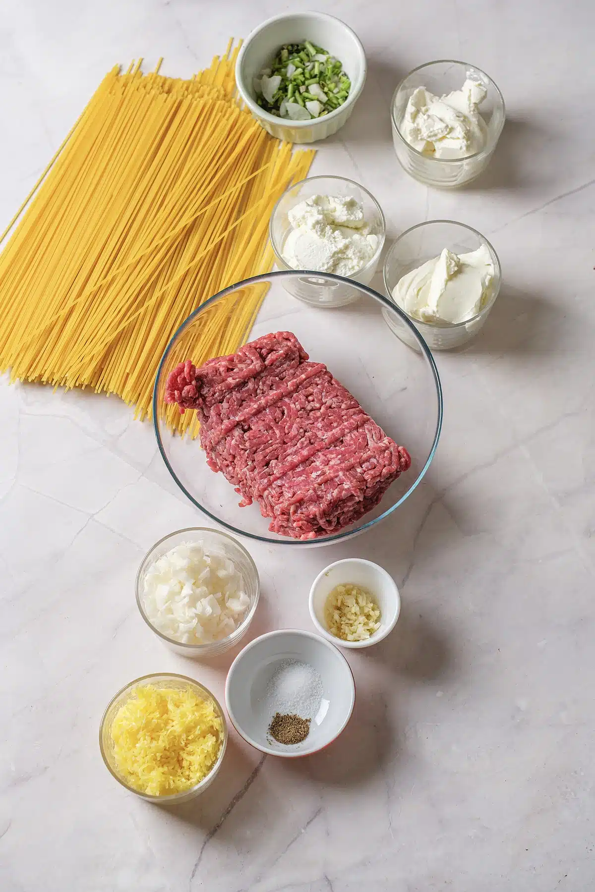 Ground beef, cream cheese, sour cream, ricotta and dry spaghetti laid out on a counter