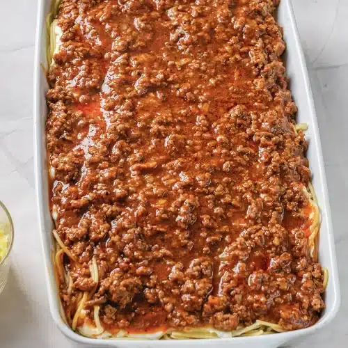 Meat sauce spread evenly over a layer of noodles in a white dish