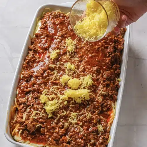 Shredded cheese tipped from a glass bowl over the meat sauce