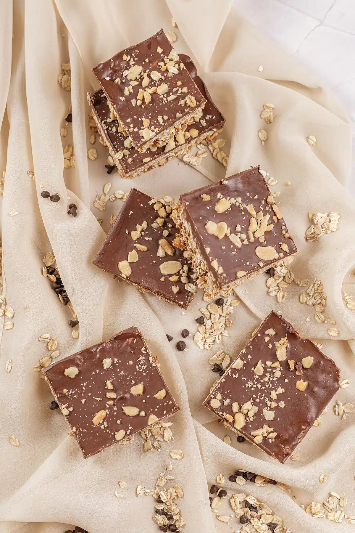 Chocolate topped squares laid out on pale fabric with scattered rolled oats