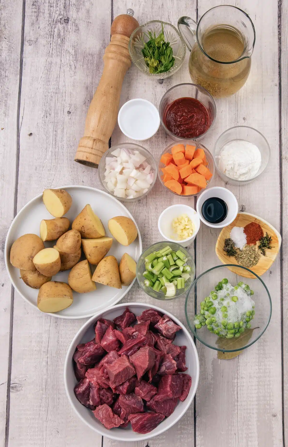 Ingredients for homemade beef stew: cubed chuck, potatoes, carrots, celery, onion, garlic, broth, oil, tomato paste, Worcestershire sauce, dried herbs, cornstarch and parsley