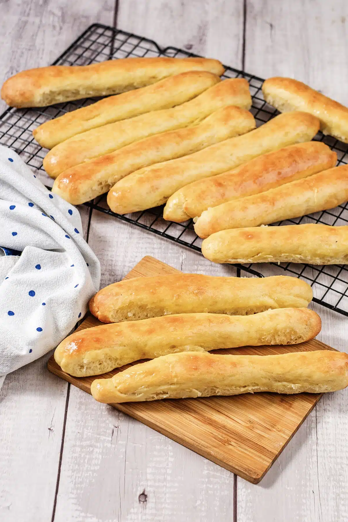 A cooling rack of baked batons with three resting on a small wooden board