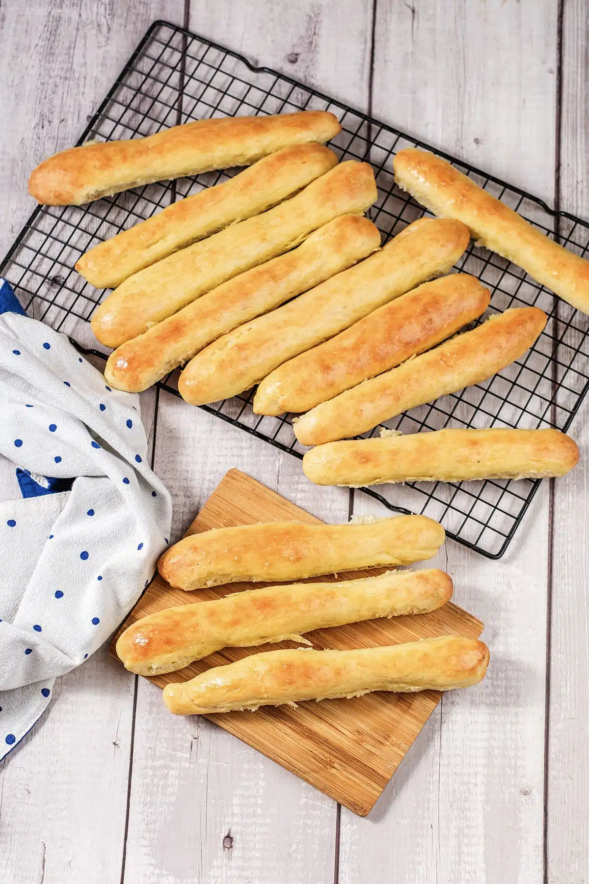 Olive Garden breadsticks cooling on a wire rack beside a wooden board