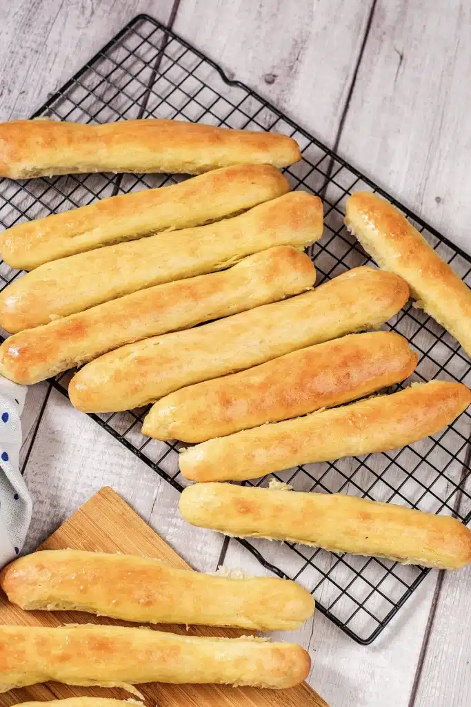 Olive Garden breadsticks stacked on a black cooling rack, seen from above