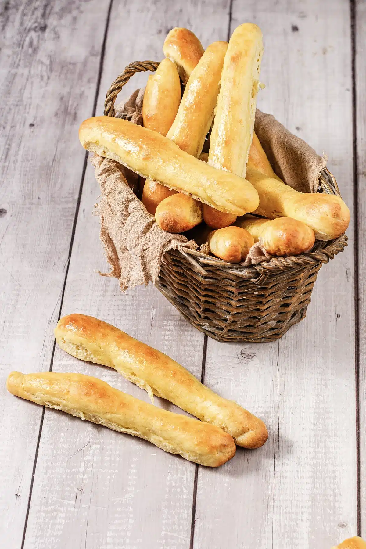 Olive Garden breadsticks piled in a woven basket with two resting in front