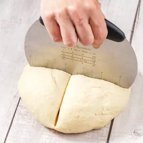 A bench scraper cutting a round of risen dough in half