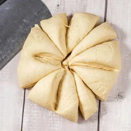 The dough round cut into twelve even wedges on a board