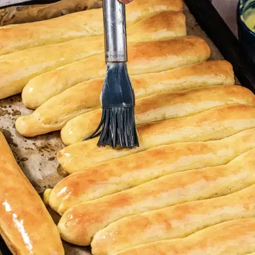 A pastry brush painting melted butter over the hot baked ropes