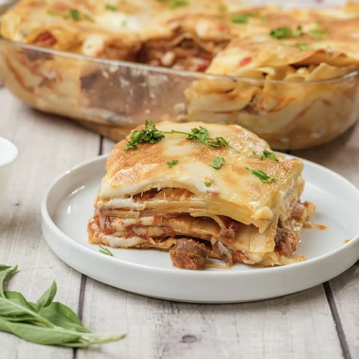 One square of Olive Garden lasagna on a white plate with the dish behind it