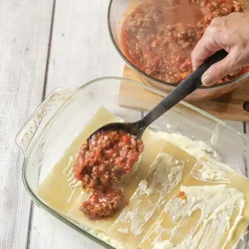 Meat sauce spooned from a bowl over the ricotta-coated noodles