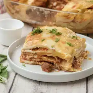 A single square of Olive Garden lasagna on a white plate with parsley on top