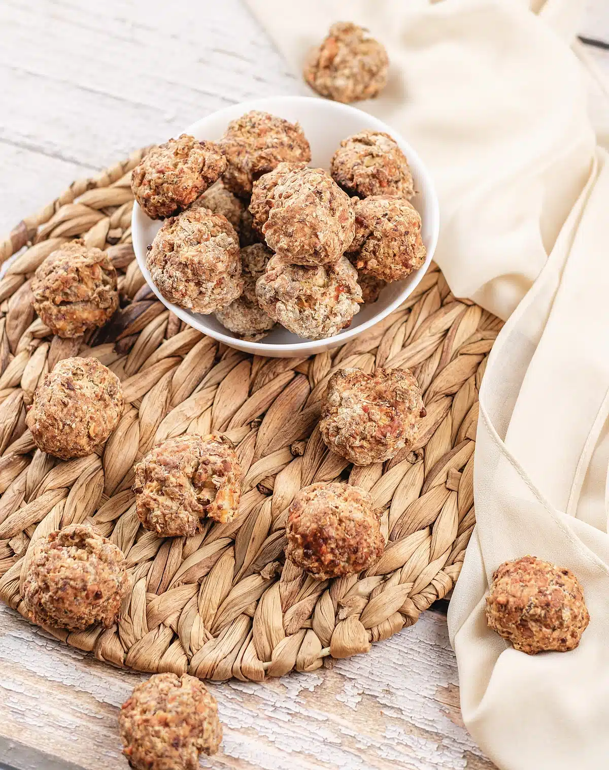 Pancake sausage balls piled in a white bowl on a woven placemat